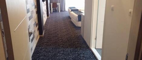 Un pasillo con alfombra estampada que lleva a una habitación con cama y sillón.