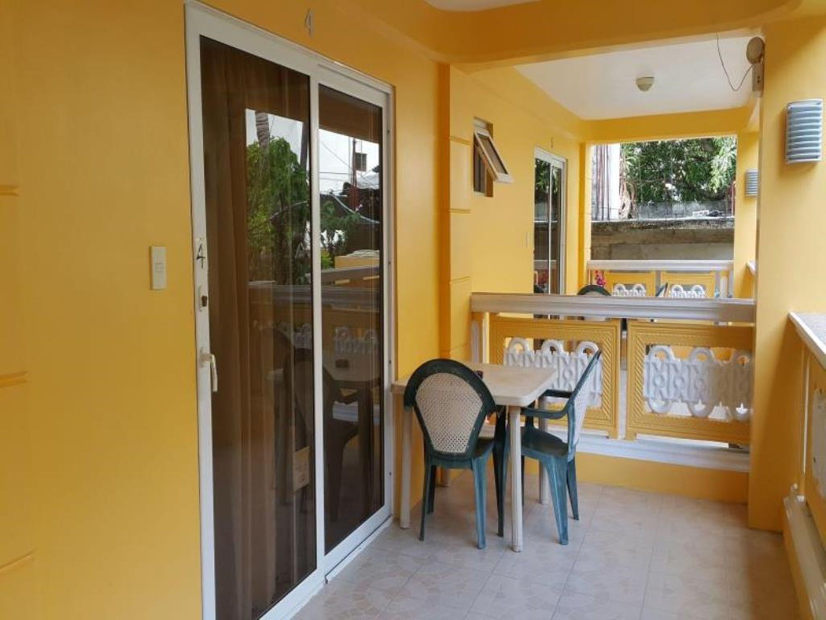 En balkon med et bord og stole, en skydedør og udsigt til gaden.