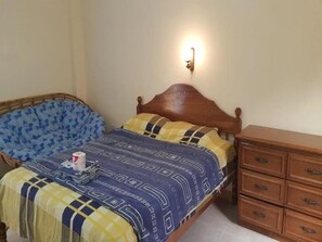A bed with a patterned bedspread, a bedside table with drawers, and a wall-mounted light fixture.