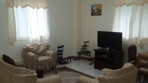 Un salon avec des fauteuils beiges, un téléviseur et une petite table.