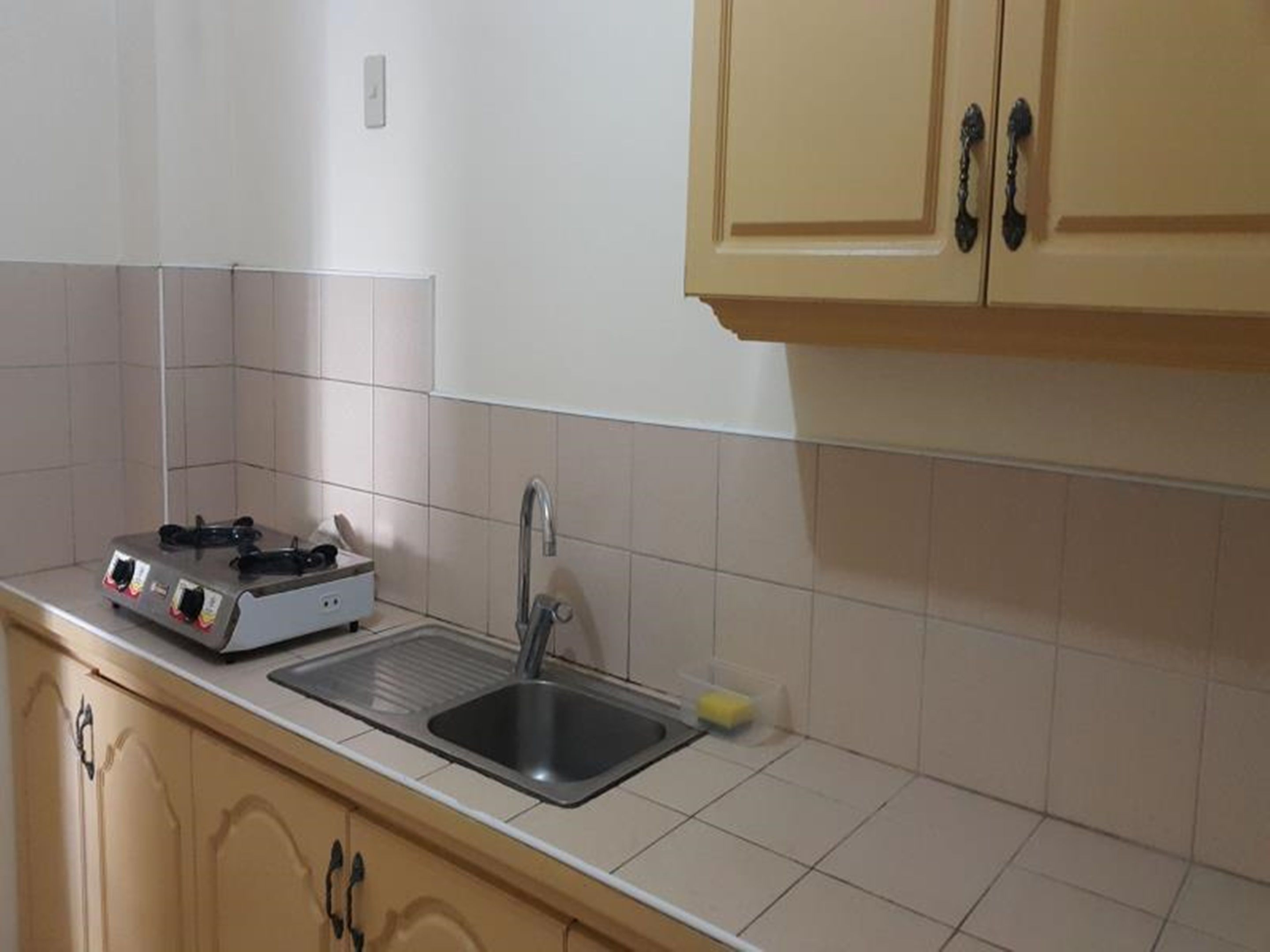 Una cocina con estufa a gas, pileta y muebles color beige.