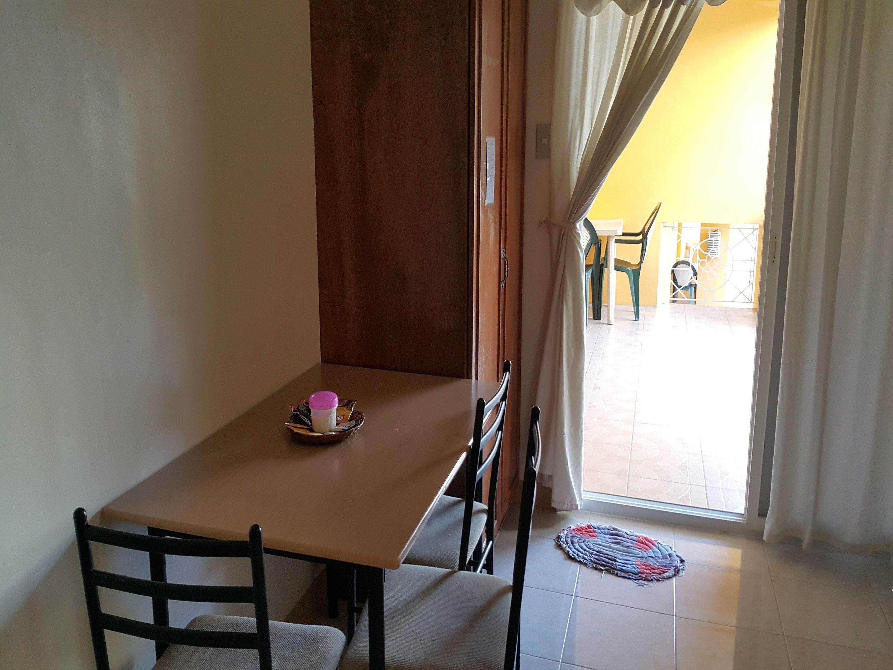 Un pequeño comedor con una mesa y sillas, una ventana con cortinas y vistas al exterior.