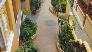 Un couloir étroit aux murs jaunes, agrémenté de plantes en pot et orné d’un élément circulaire central.