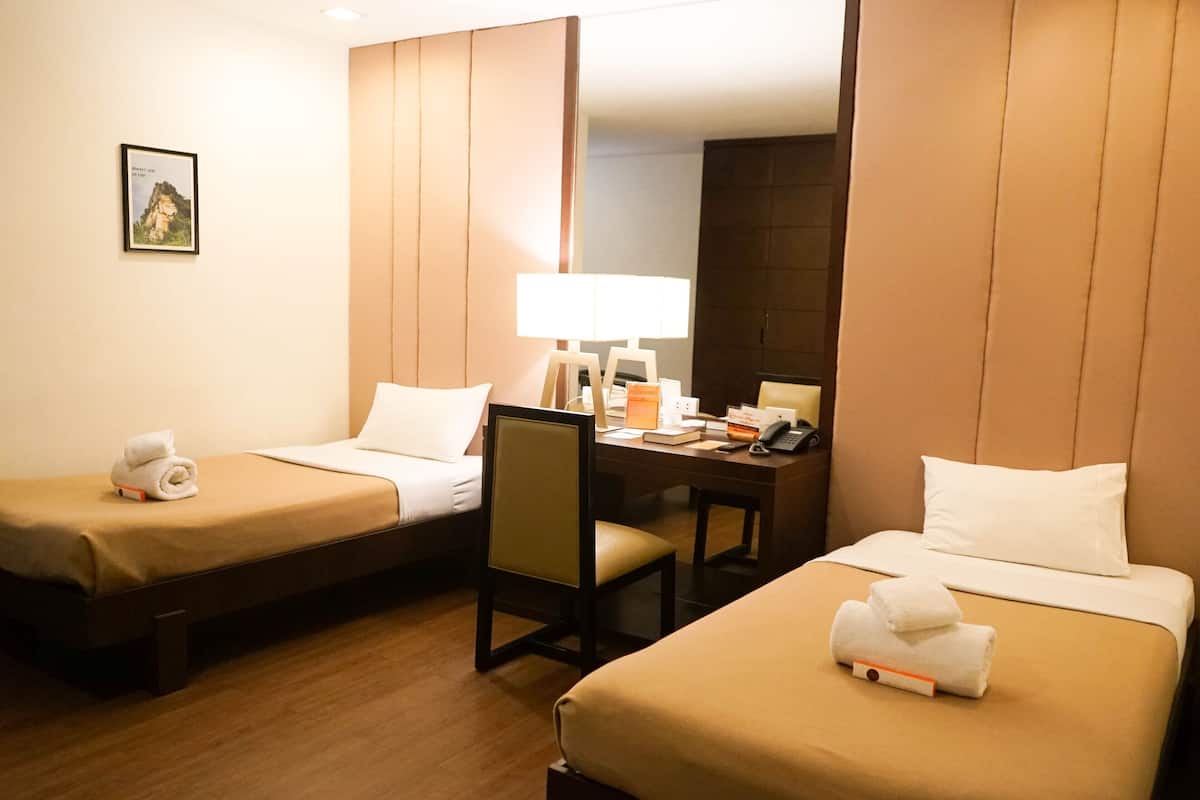 Habitación de hotel con dos camas individuales, un escritorio con silla, una lámpara y un teléfono.