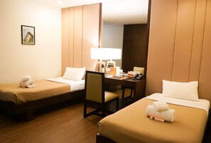 Une chambre d’hôtel avec deux lits simples, un bureau avec une chaise, une lampe et un téléphone.
