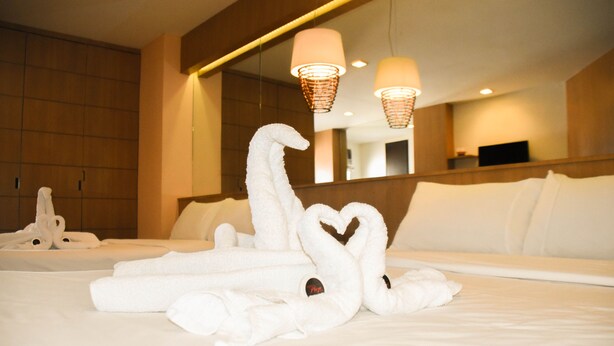 Habitación de hotel con una cama bien hecha, un espejo grande y una lámpara de pared.