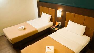 Two single beds with brown headboards and white linens, a bedside table with a lamp, and a folded towel on the floor.