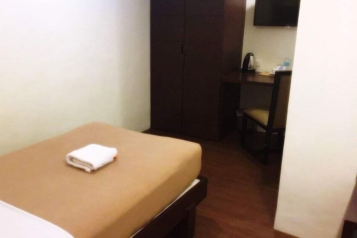 Una habitación de hotel pequeña con una cama individual, una mesita de noche de madera, una silla, un escritorio y una televisión.
