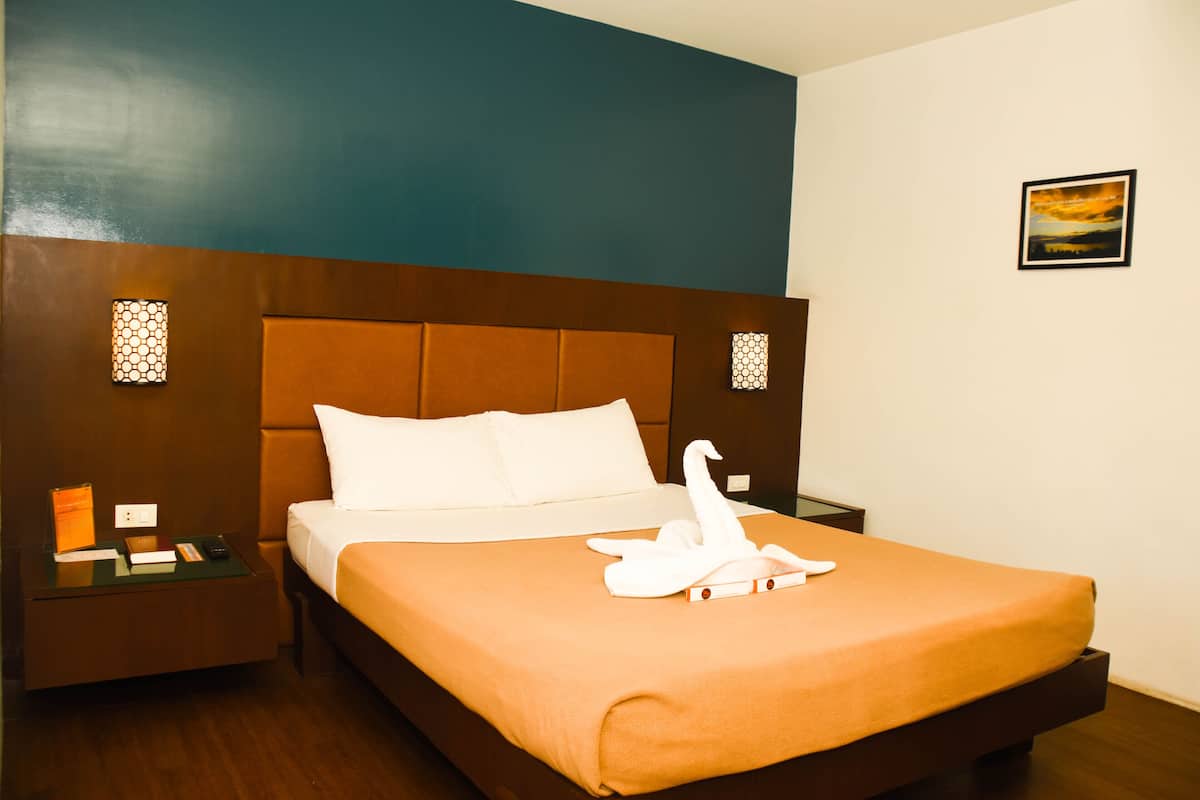 Una habitación de hotel con una cama grande, una mesita de noche y una lámpara fijada a la pared.