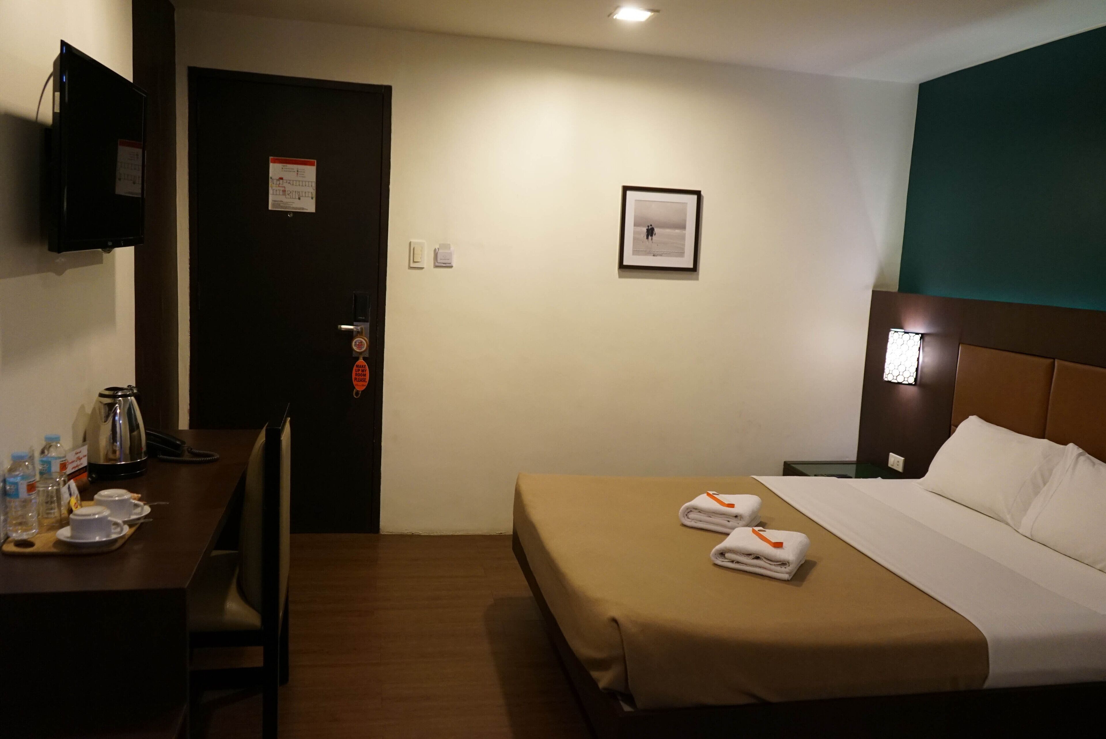 A hotel room with a bed, a desk with a kettle, and a television.