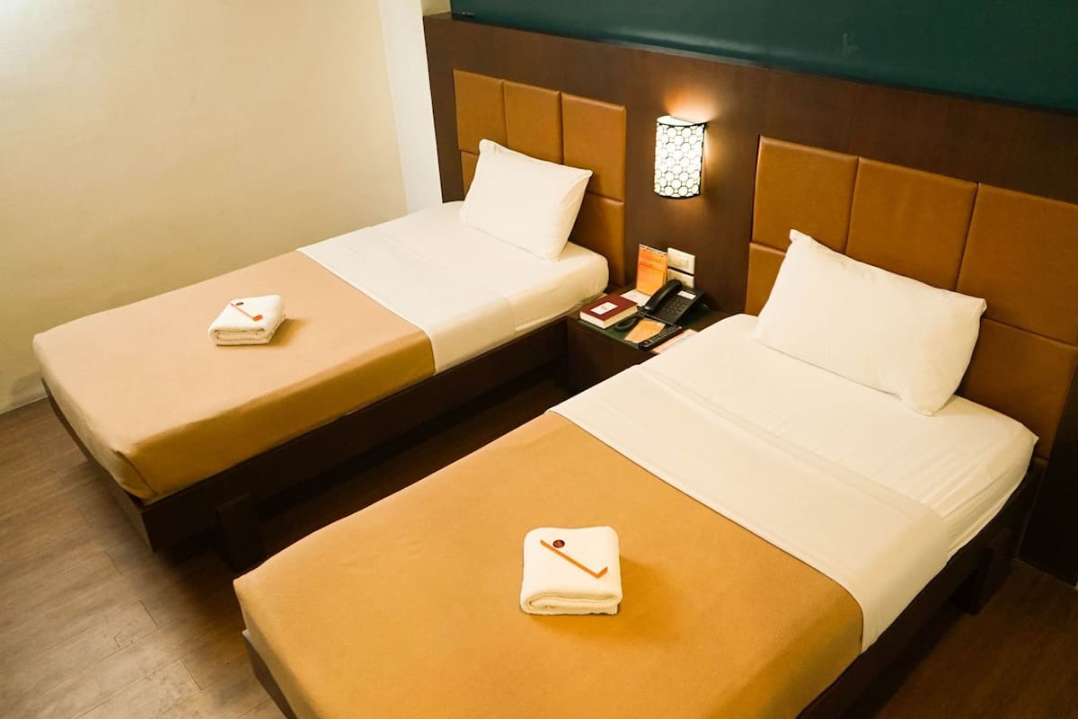 Una habitación de hotel con dos camas, una mesita de noche con lámpara y suelo de madera.