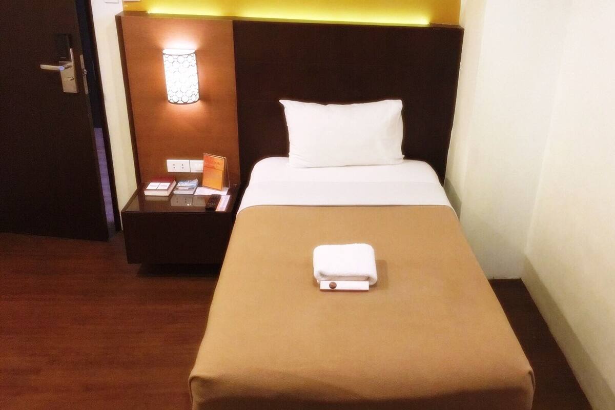 Una habitación de hotel con una cama individual, una mesita de noche con lámpara y un cartel de bienvenida.