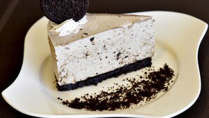 Una porción de pastel de queso con una galleta encima, servida en un plato blanco.