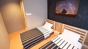 A room with two beds, a nightstand, a wall-mounted painting of a tree and sky, and a door. - Koptel Budget Hotel (Kuching)