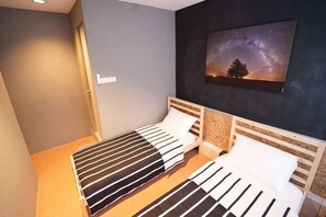 Et værelse med to senge, et natbord, et billede af et træ og himlen på væggen, samt en dør.