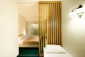 A hotel room with a bed, a bedside table, a wooden partition, and a wall-mounted light fixture. - Mayo Inn (Singapore)