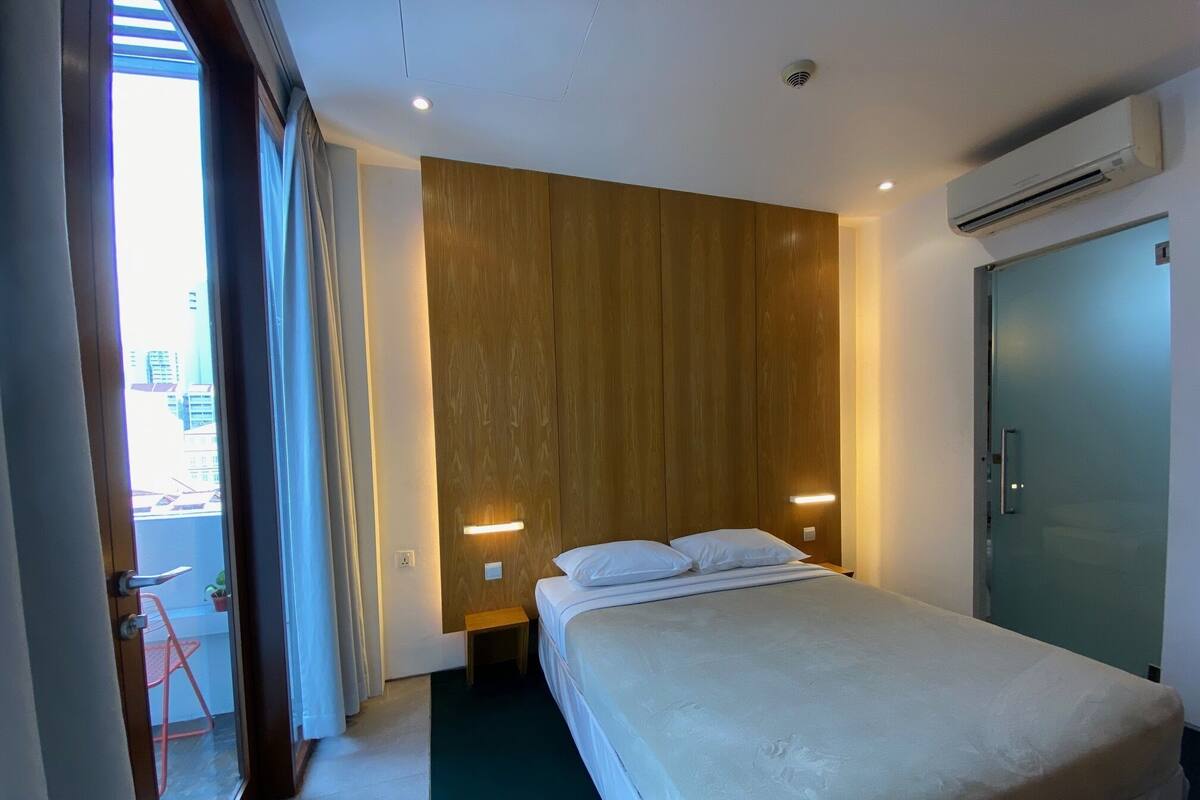 Habitación de hotel con una cama grande, panel de pared de madera y vista de la ciudad a través de una ventana.