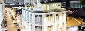 A multi-story building with a prominent corner entrance, a visible ground floor with a parking area, and a series of windows with shutters. - Mayo Inn (Singapore)