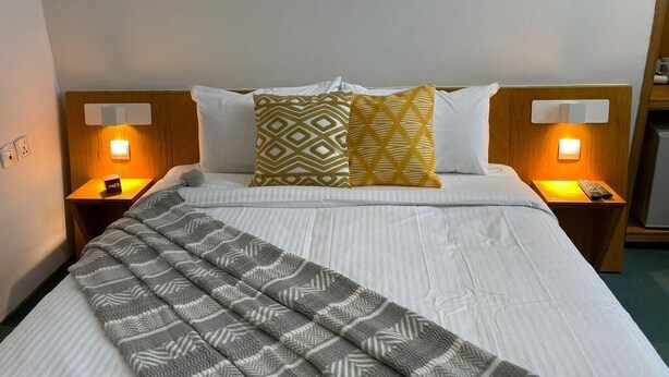 Una cama bien hecha con un edredón estampado, dos mesitas de noche con lámparas y una luz instalada en la pared.