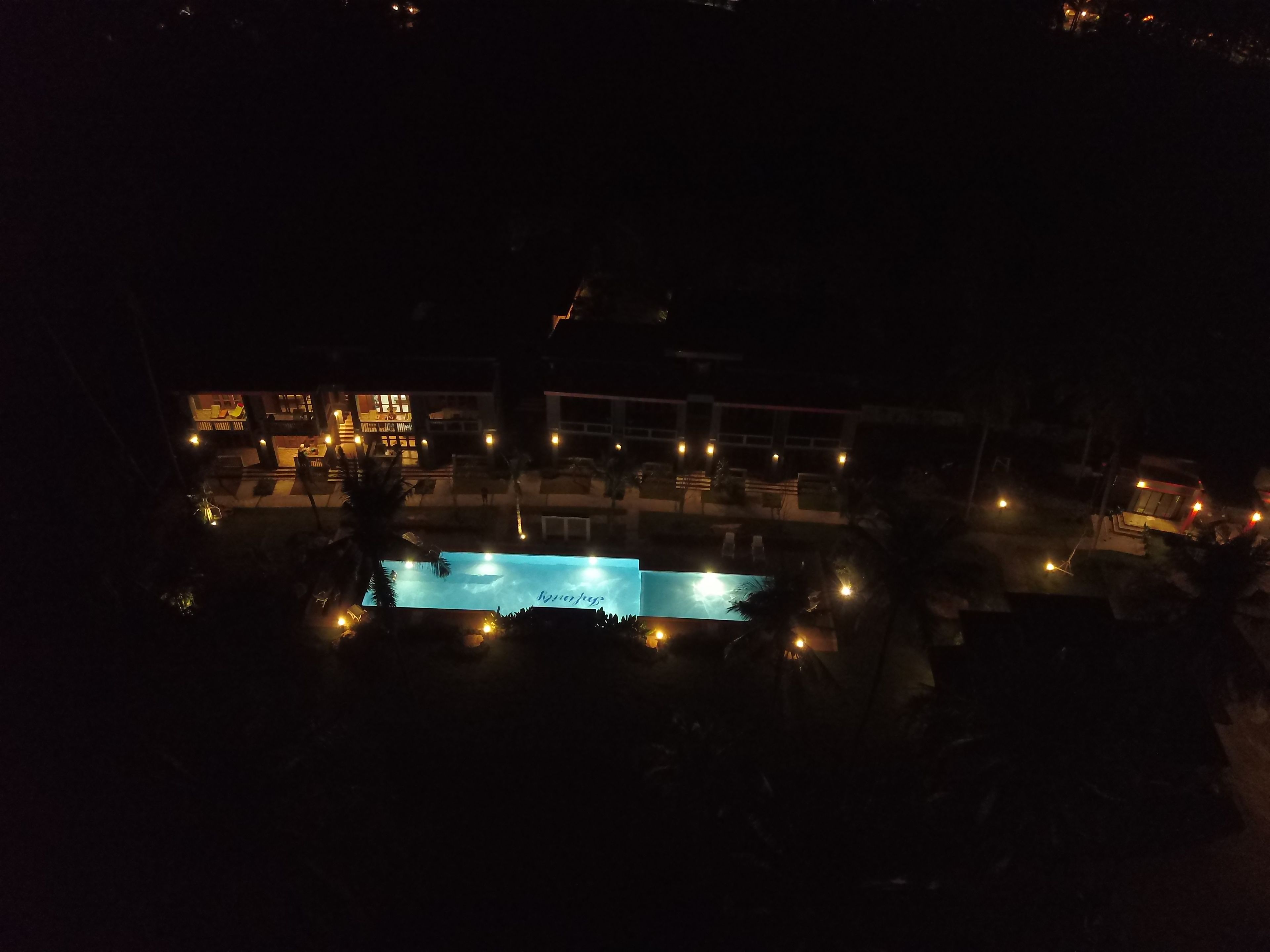 A nighttime view of a resort with a pool area, outdoor seating, and illuminated buildings.