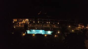 A nighttime view of a resort with a pool area, outdoor seating, and illuminated buildings.