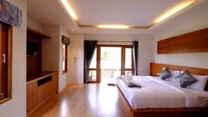 A hotel room with a wooden bed, a TV, a desk, and a balcony with a view. - Lanta Infinity Resort (Ko Lanta)