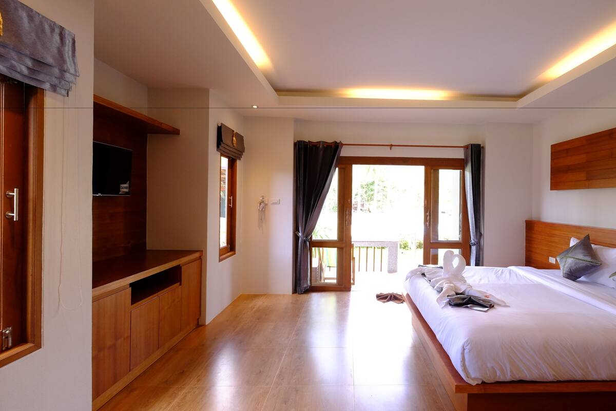 Une chambre d’hôtel avec un lit en bois, une télévision, un bureau et un balcon avec vue.