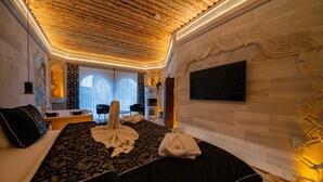 A hotel room with a wooden ceiling, a large bed with a patterned bedspread, a flat-screen TV mounted on the wall, and a window with curtains. - Safran Cave Hotel (Nevsehir)