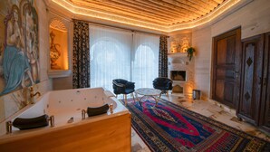 A luxurious bathroom with a freestanding bathtub, two armchairs, a patterned rug, and a decorative fireplace. - Safran Cave Hotel (Nevsehir)