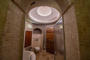 A narrow, tiled bathroom with a skylight, a toilet, and wooden cabinets.