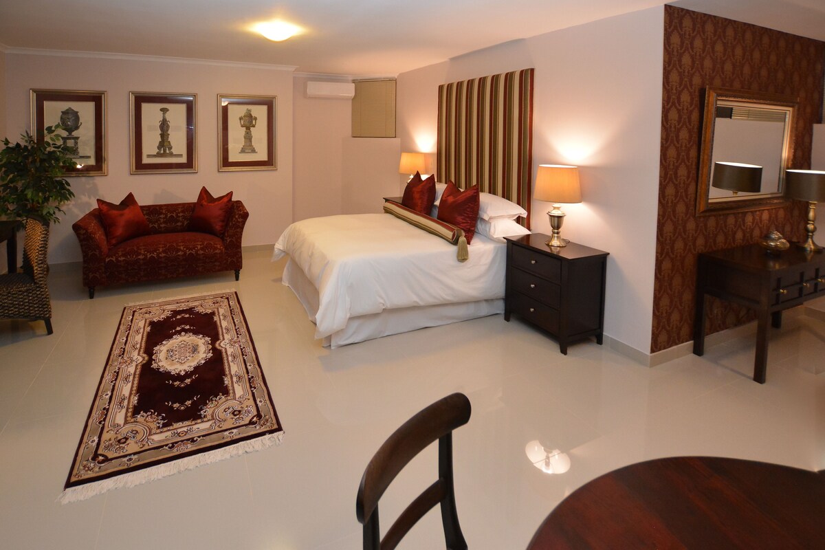 A hotel room with a bed, a sofa, a nightstand, a mirror, and a large rug.