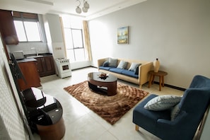 A living room with a sofa, coffee table, and a small side table. There is a kitchen area with a stove and cabinets.