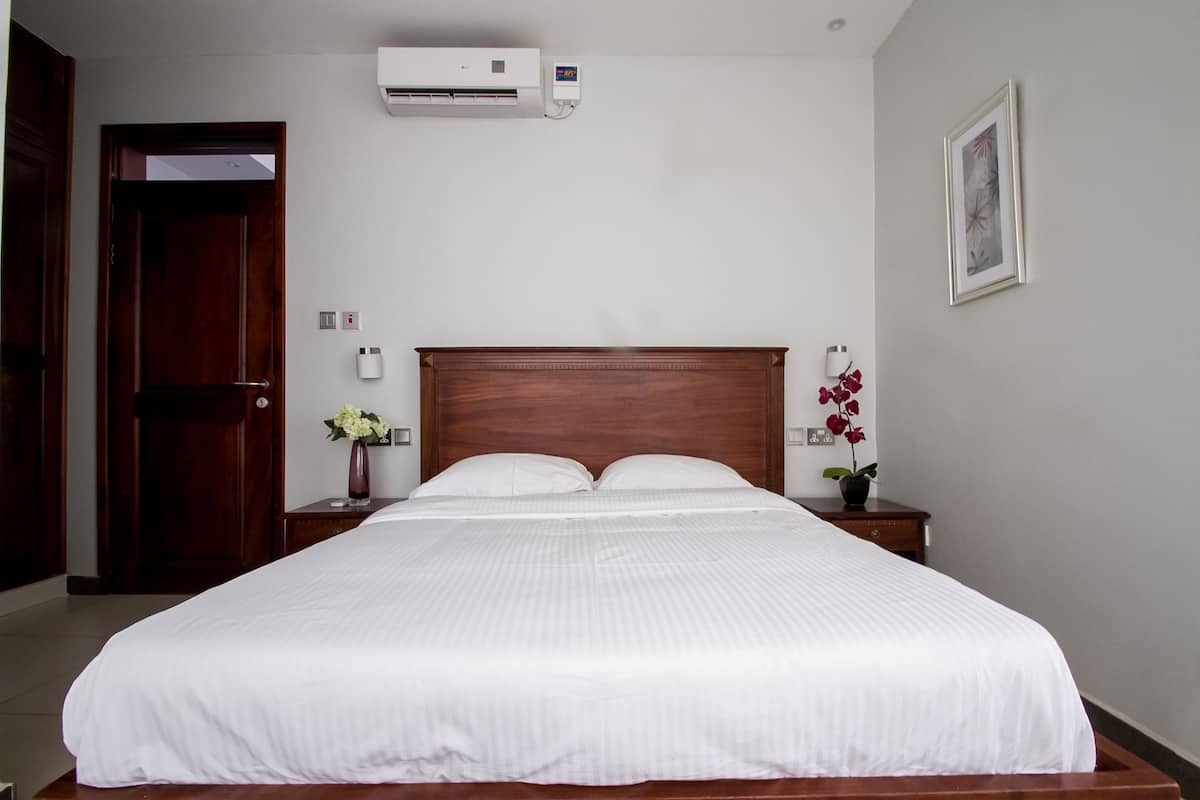 A neatly made bed with white bedding, a wooden headboard, and two bedside tables with flower vases.
