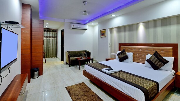 A hotel room with a large bed, a TV, a small table, and a sofa. - Hotel Emporio (New Delhi)