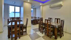 A dining area with wooden tables and chairs, a checkered floor, and an air conditioning unit on the wall. - Hotel Emporio (New Delhi)