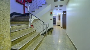 A staircase with granite steps and metal railings, leading to a hallway with a door marked "EXIT" and a fire extinguisher mounted on the wall. - Hotel Emporio (New Delhi)