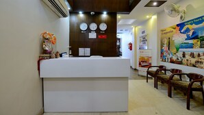 A reception desk with clocks, a fire extinguisher, and a wall with travel information posters. - Hotel Emporio (New Delhi)