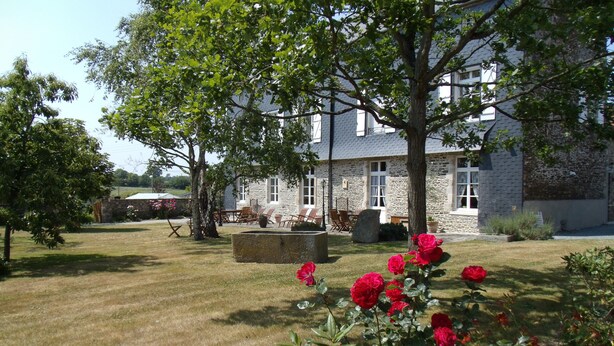 A stone building with a garden in front, including a stone fountain and red roses. - Le Tertre (La Feuillie)