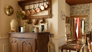 A traditional kitchen with wooden cabinets, a hanging pot rack, and a dining area with a table and chairs. - Le Tertre (La Feuillie)