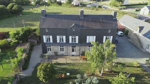A two-story stone house with a dark roof, white shutters, and a paved driveway. - Le Tertre (La Feuillie)