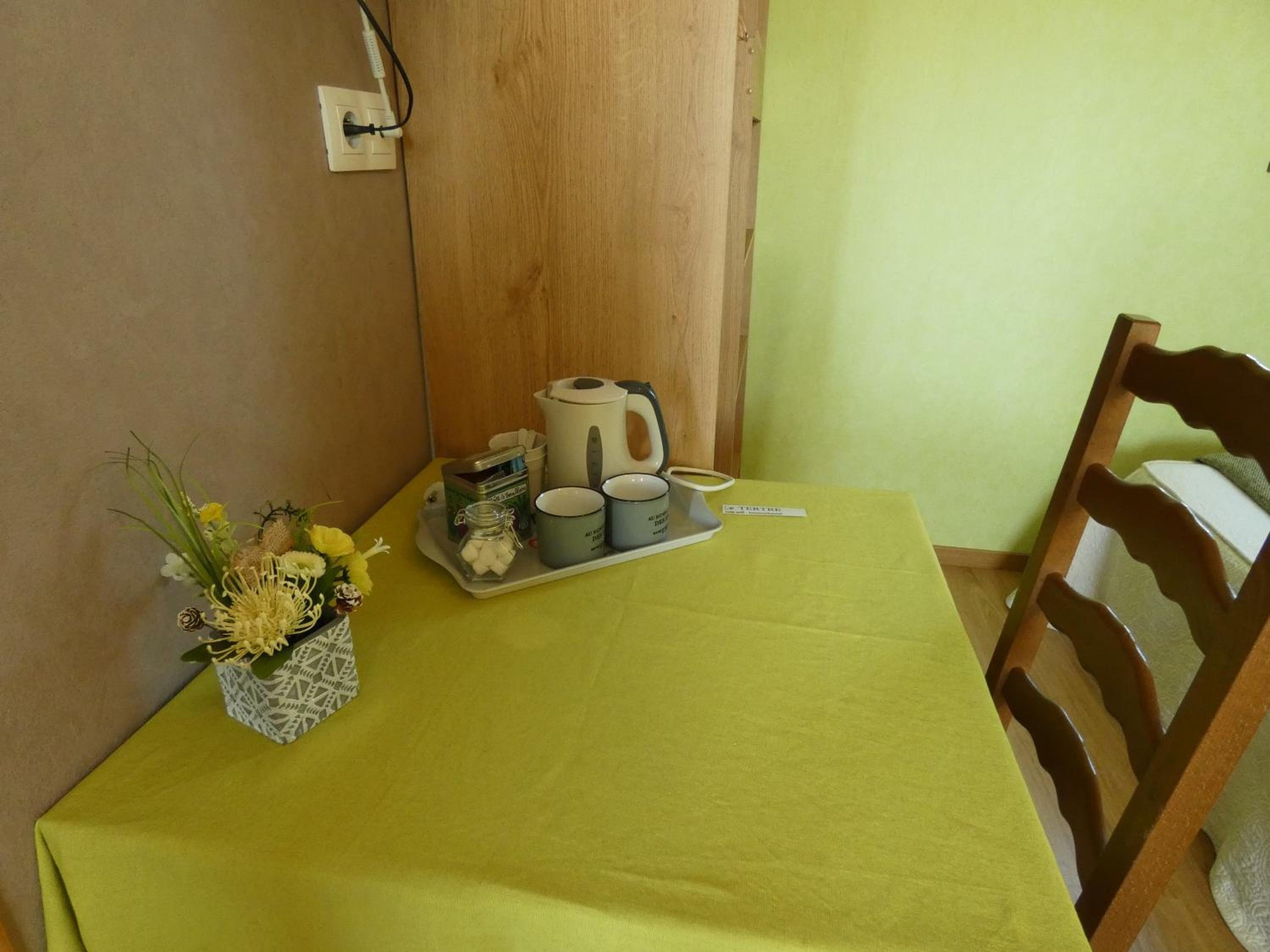 A small table with a green tablecloth, a coffee maker, cups, a tray, and a vase with flowers.