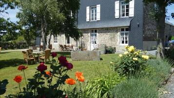 A stone building with a garden in front, outdoor seating, and a clear sky.