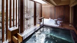 Un jacuzzi con barandas de madera, un pequeño banco de madera y una silla en una habitación con piso de madera y vista a un paisaje nevado.