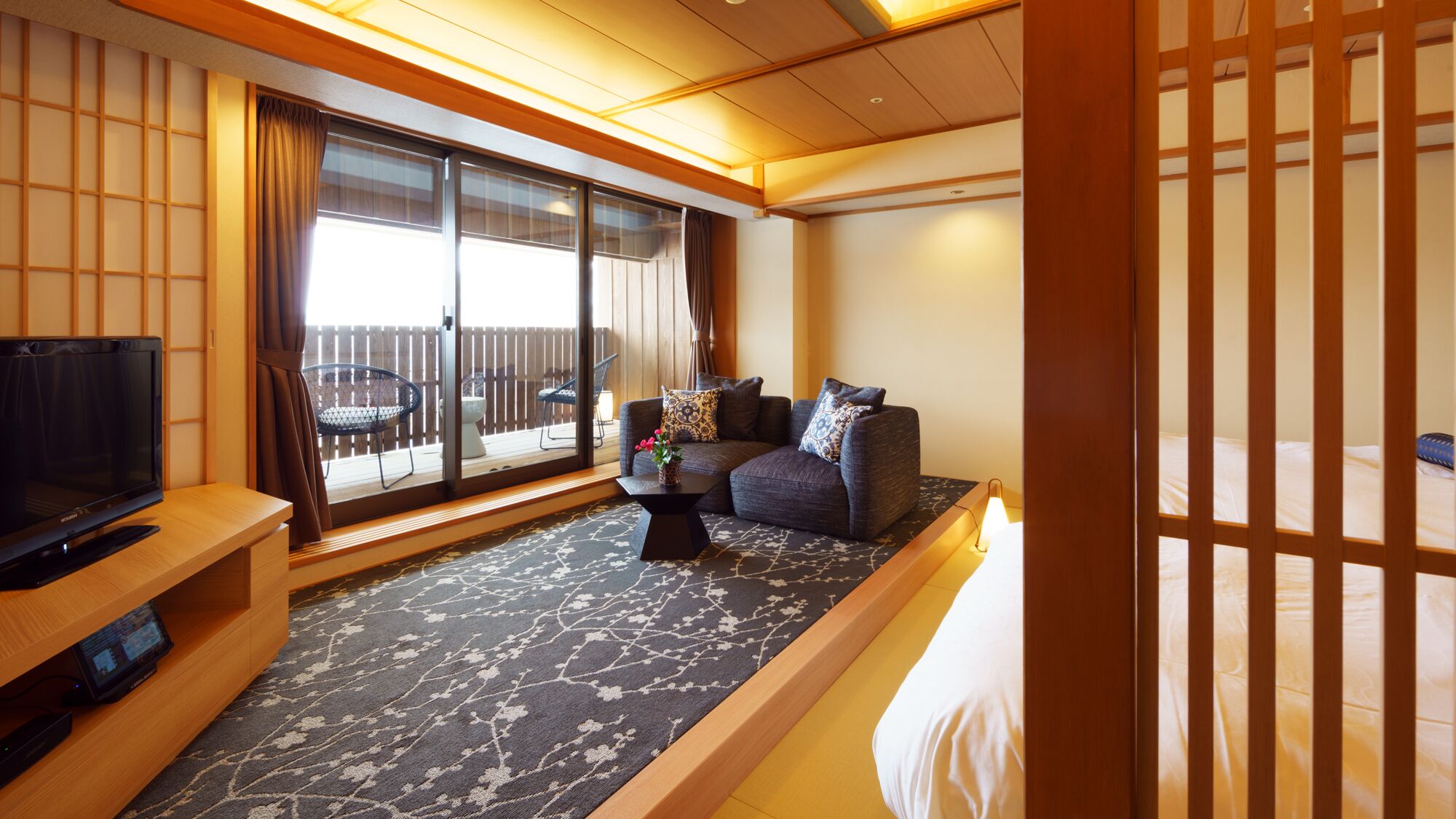 Ein Hotelzimmer mit einer Couch, einem Fernseher, einem kleinen Tisch und Blick ins Freie.