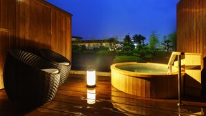 Una terraza de madera con un jacuzzi y un farolillo, con vistas a un jardín y edificios.