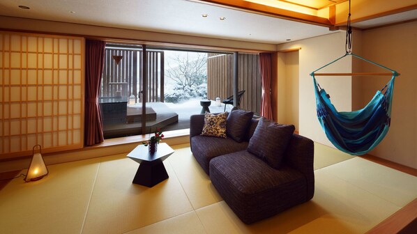 A modern living room with tatami flooring, a sofa with cushions, a hanging hammock, and a view of a snowy outdoor deck.
