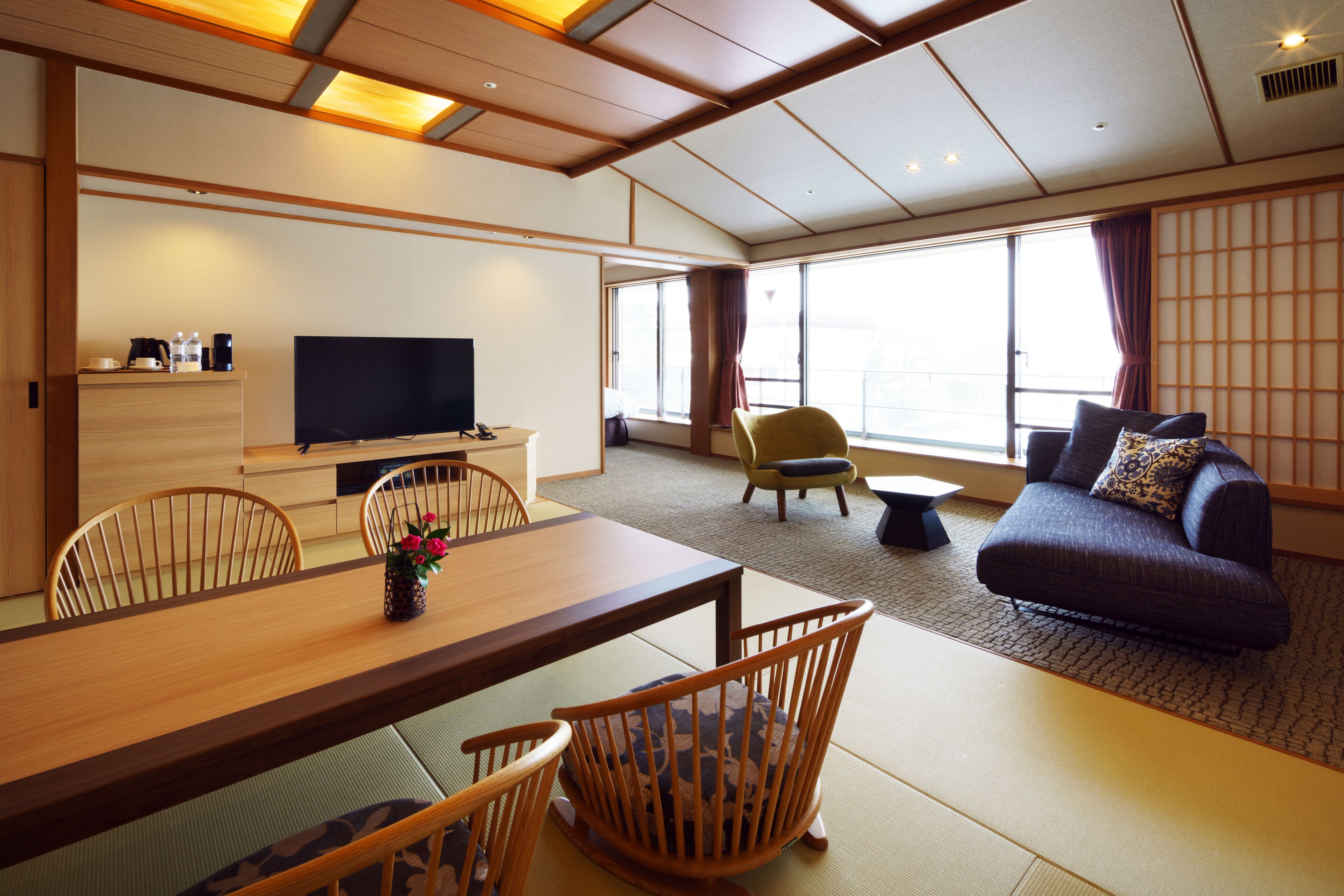Een moderne hotelkamer met een houten eettafel, stoelen, een bank en een televisie.
