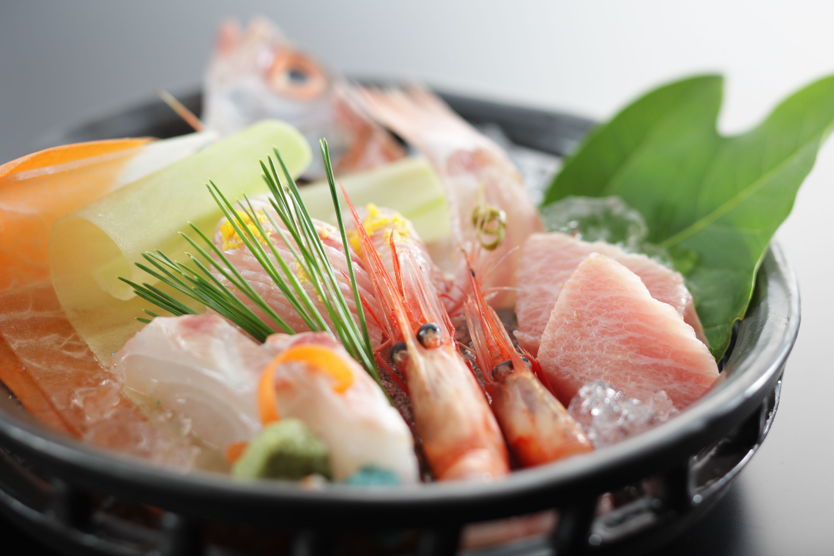 A variety of seafood including shrimp, salmon, and other fish, arranged on a bed of ice in a black bowl.