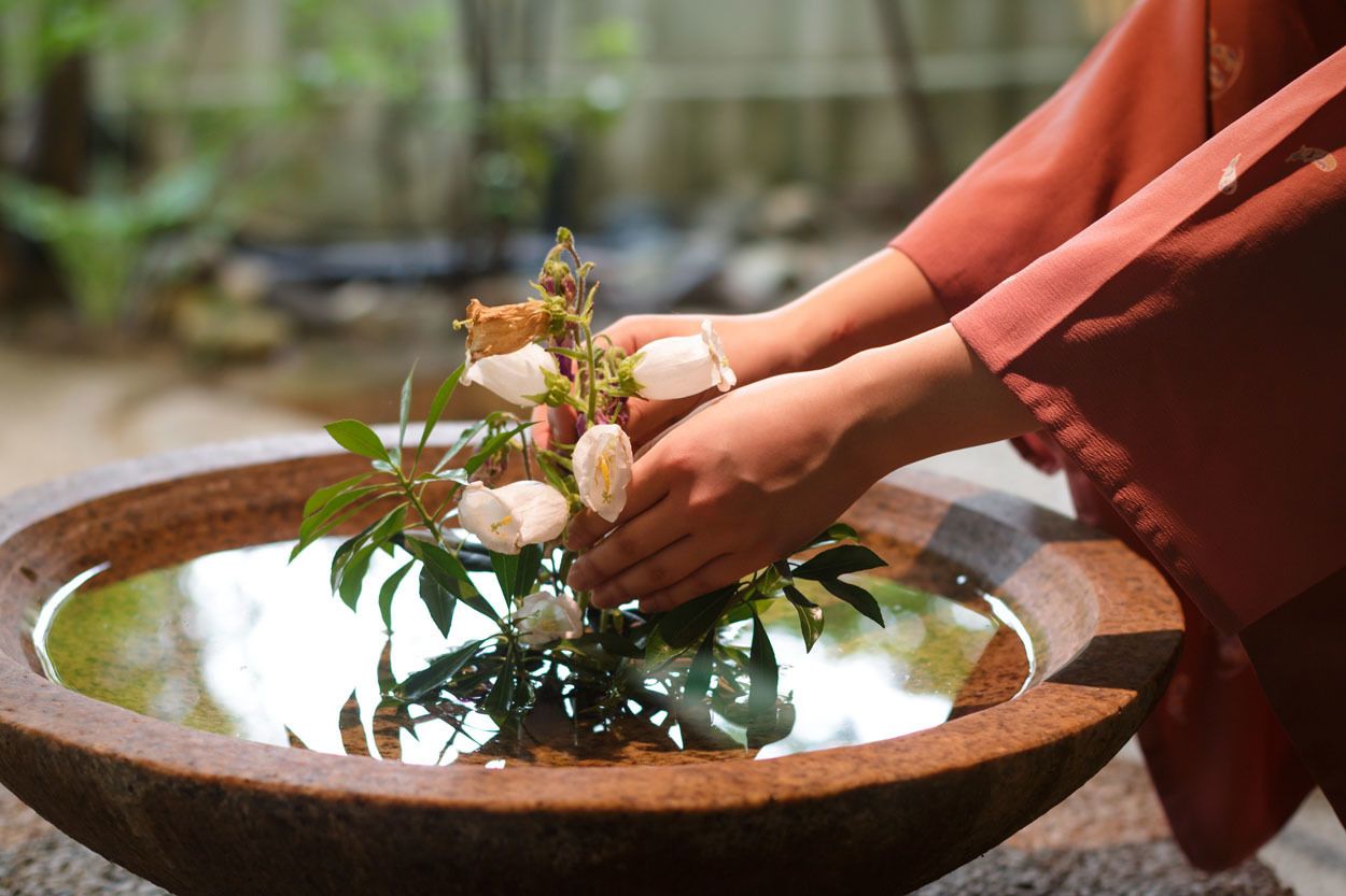 Eine Person legt Blumen in eine steinerne Schale mit Wasser.