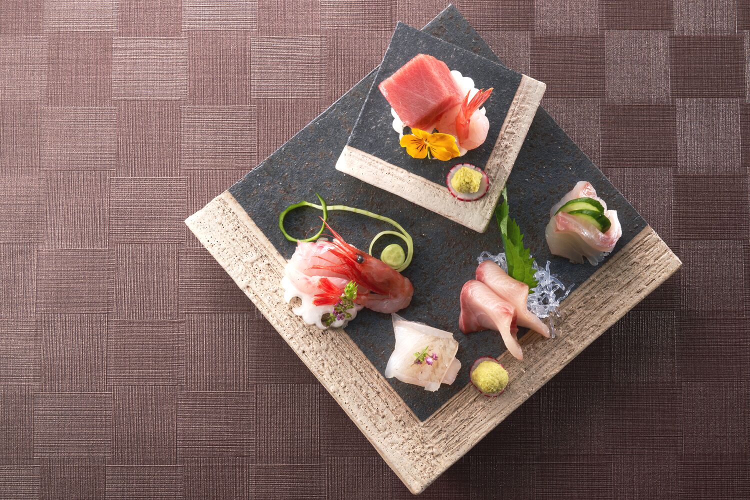 A sushi platter with various types of fish and garnishes on a slate board.